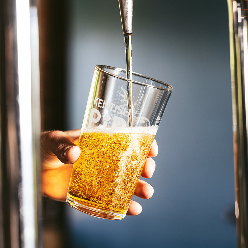 A hand holding a pint, pouring hand crafted cider from a draught in a bar